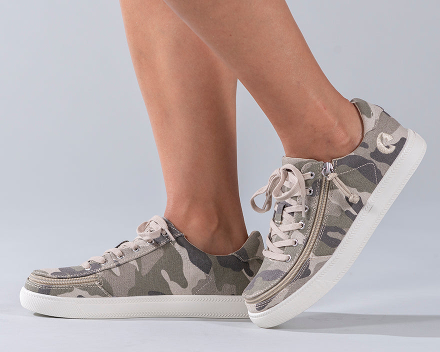A person wearing Women's Natural Camo BILLY Classic Lace Lows, featuring camouflage design, adjustable laces, and rubber tread outsole.