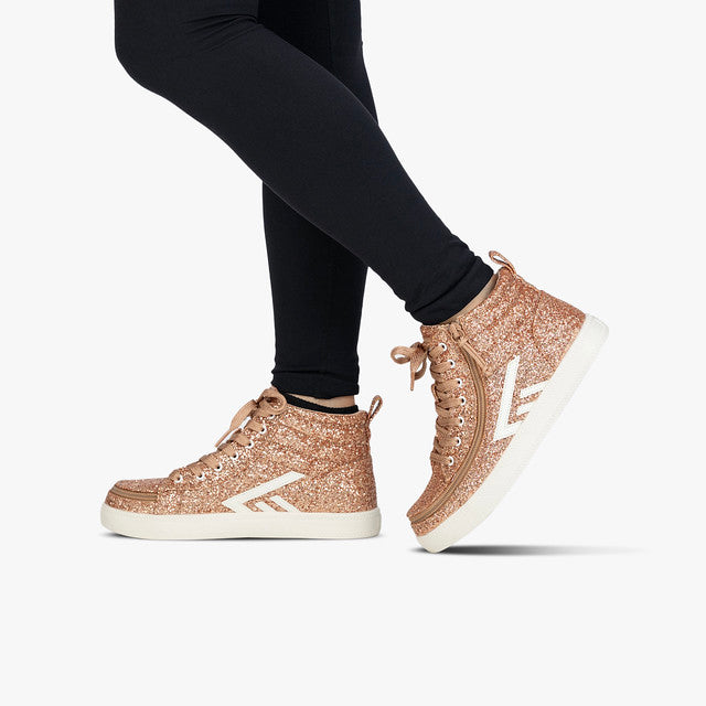 Person wearing Billy Footwear - Rose Gold Glitz CS Canvas Shoes with black pants, featuring high tops, glitter finish, laces, and wraparound zipper for easy access.